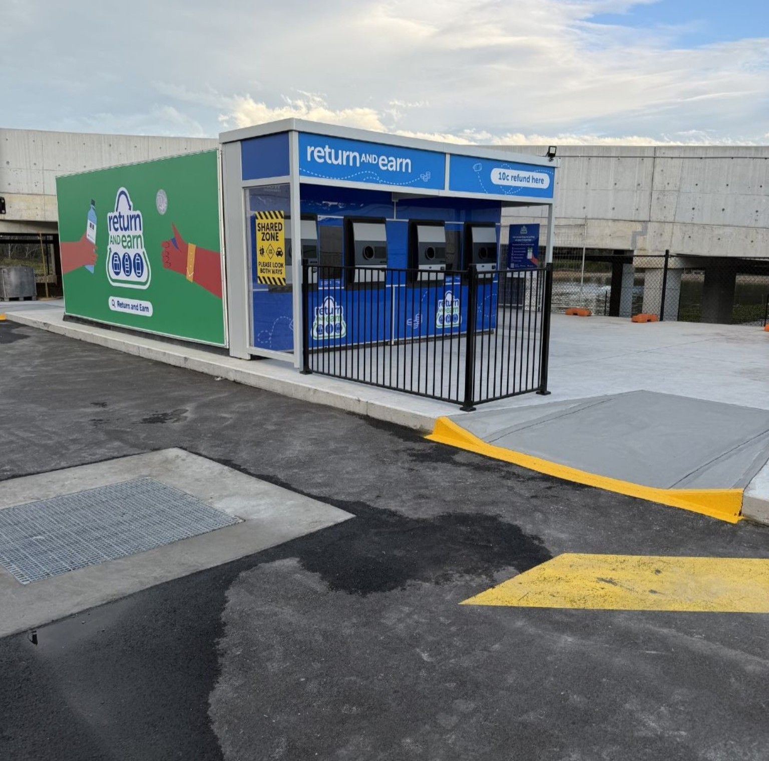 Outdoor Return and Earn site with three reverse-vending machines and a storage enclosure